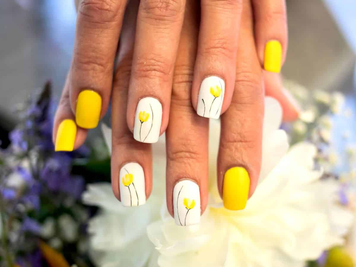 A woman's hands adorned with vibrant yellow and white nails showcase her fashionable yet sophisticated style.