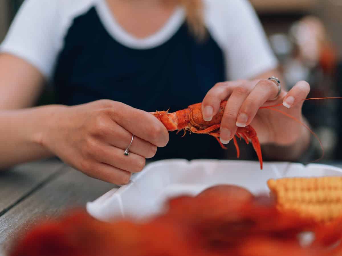 A woman is peeling a piece of crawfish on a plate.
