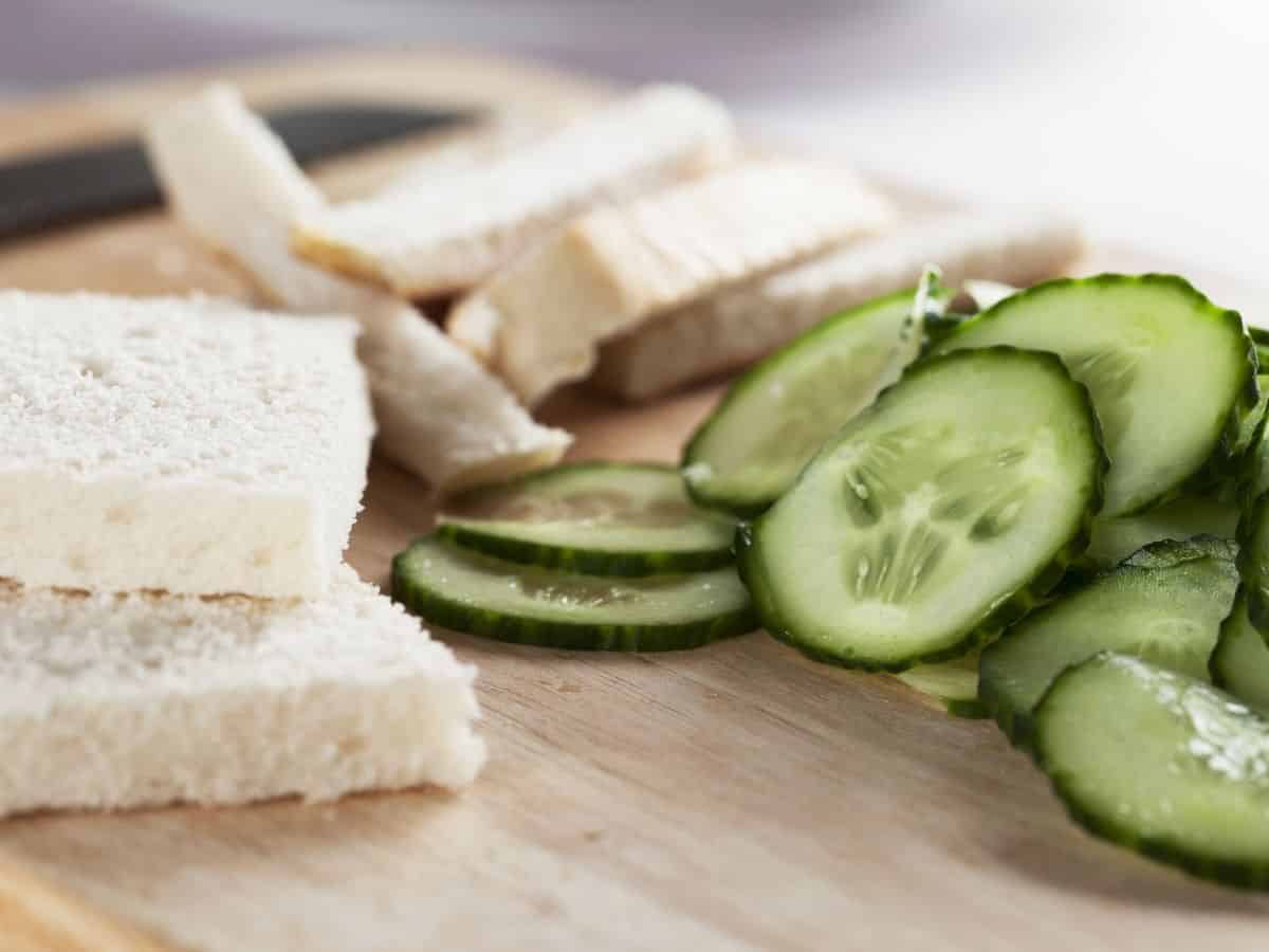 Sliced bread and cucumbers on a cutting board ready for cucumber sandwiches.