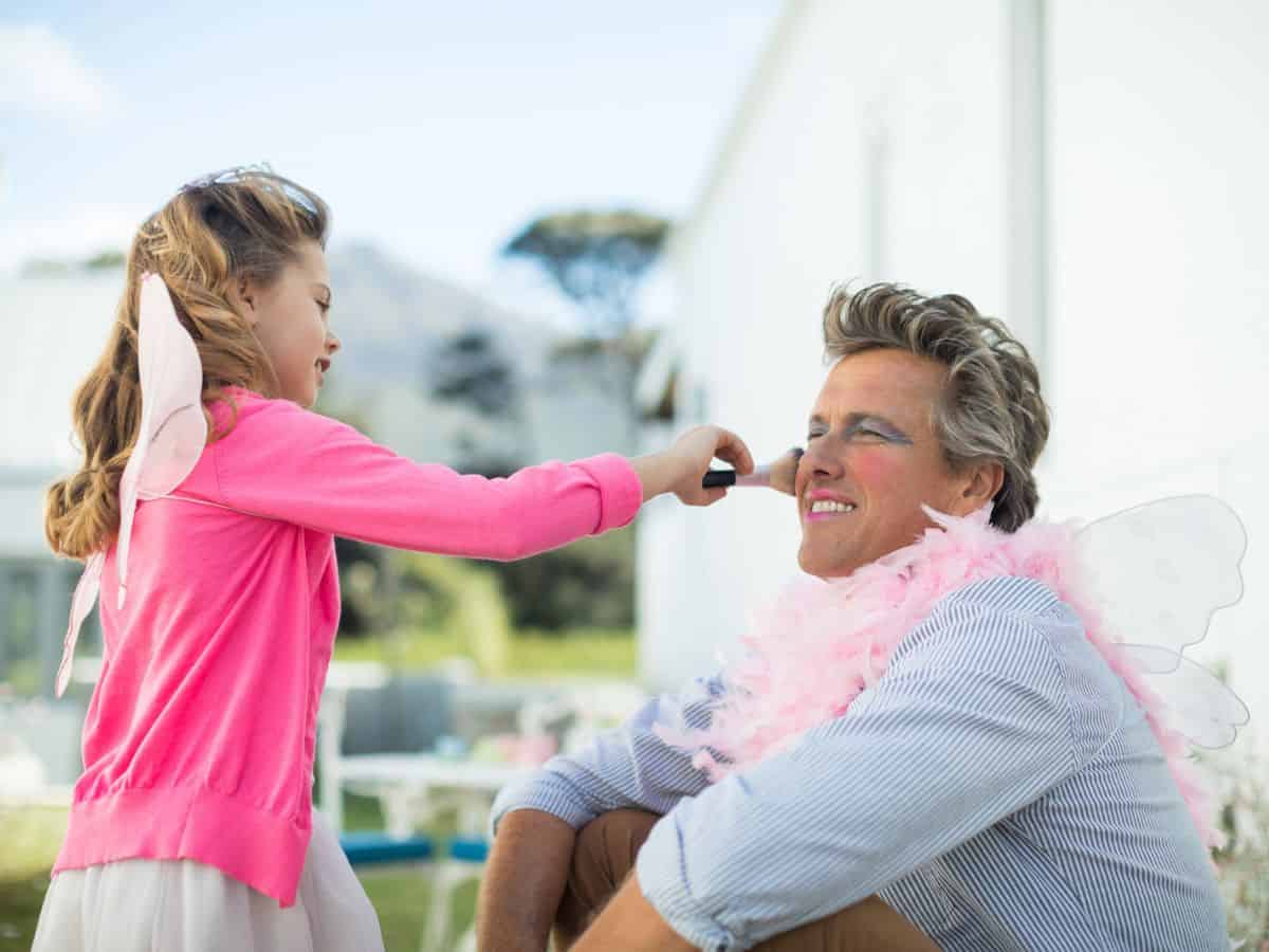 A young girl applying make-up to her father's face.