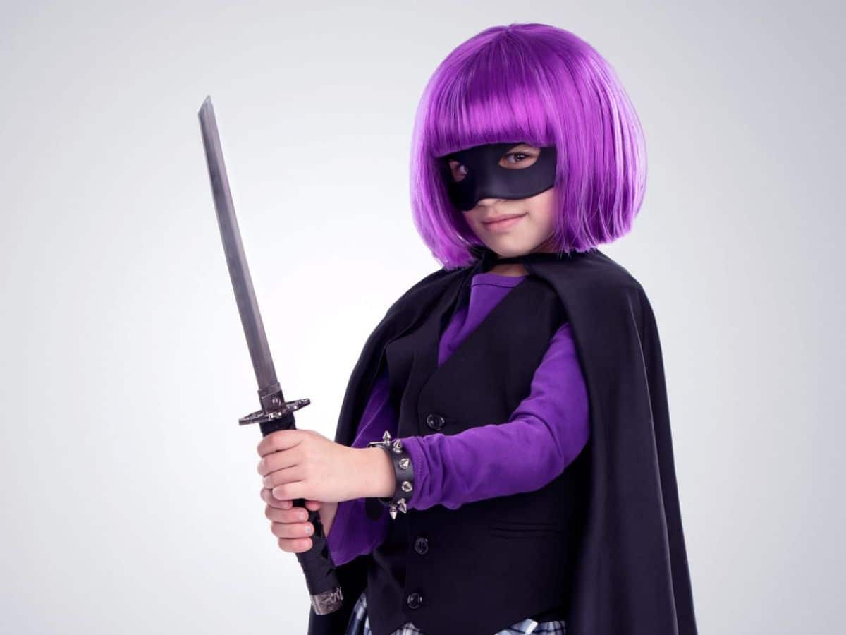 A little girl in a purple Mardi Gras costume holding a sword.