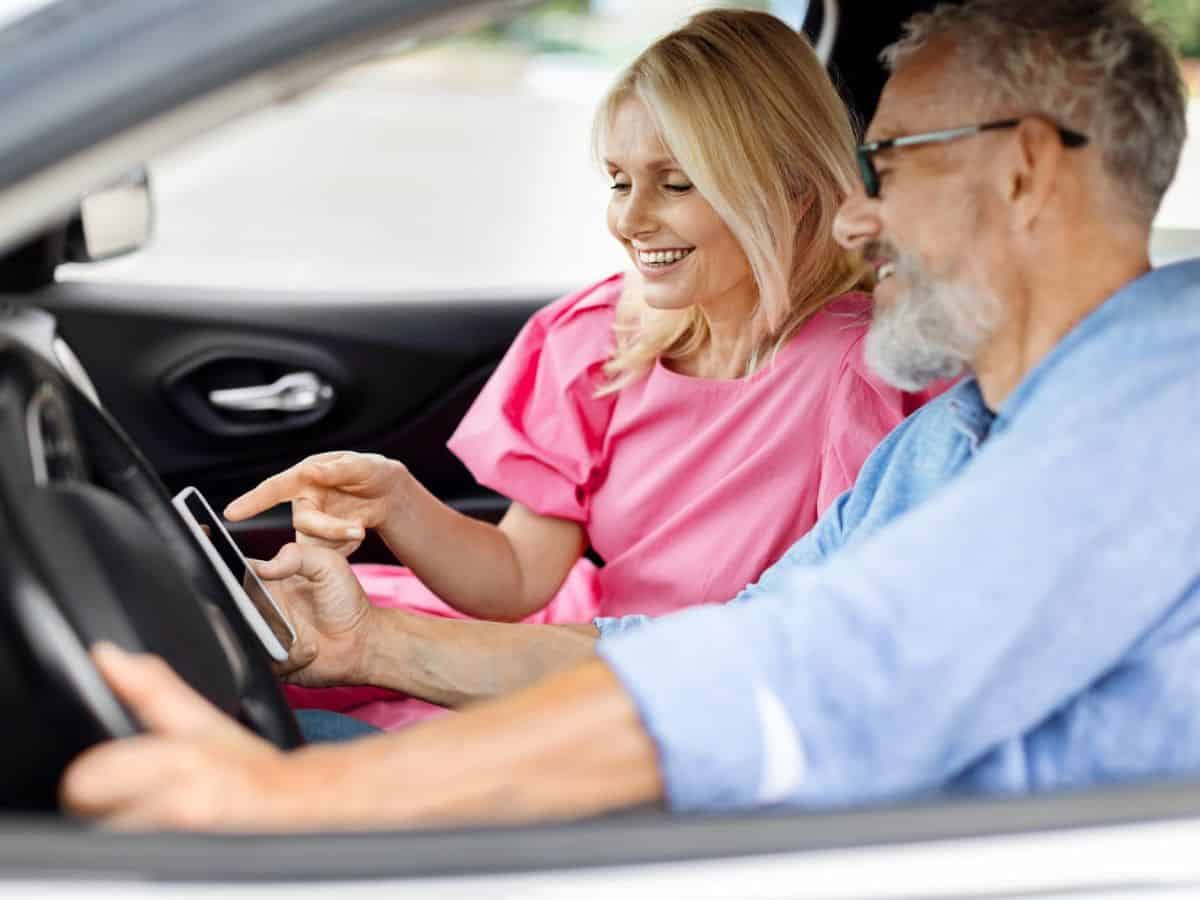 A man and woman in a car looking at a road map on a phone.