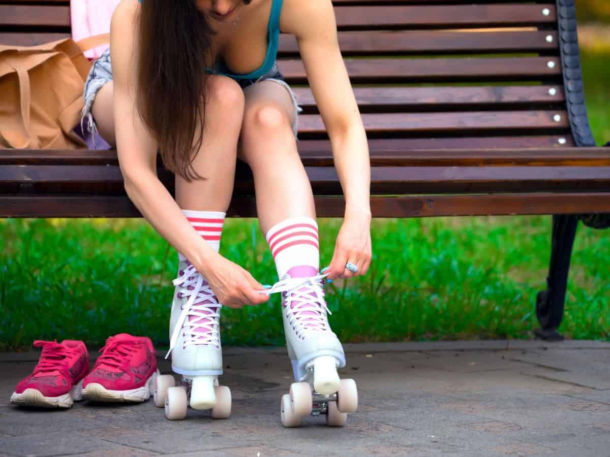 A woman sitting on a bench tying the laces of her roller skates.