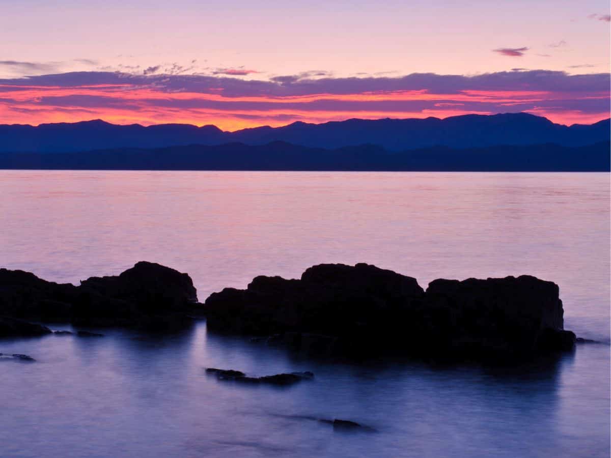 Sunrise over Flathead Lake with rocks in the foreground.