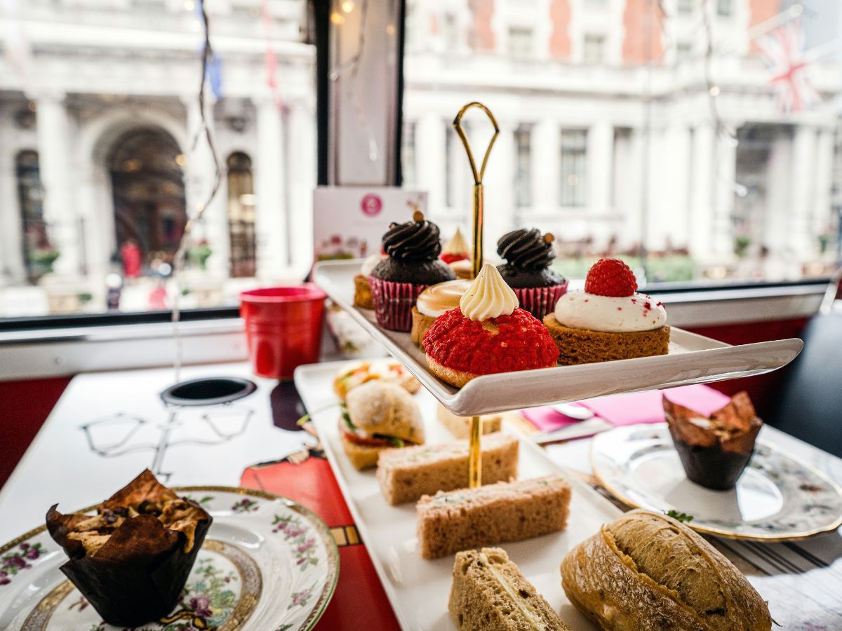 Afternoon tea selection with desserts and sandwiches served on a tiered stand, with a city view from a window in the background.