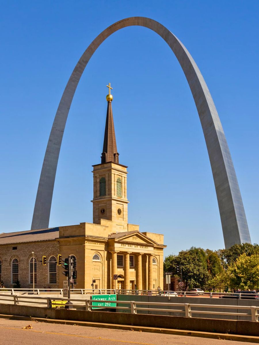 The gateway arch towers behind the steeple of the Basilica of St. Louis in Missouri.