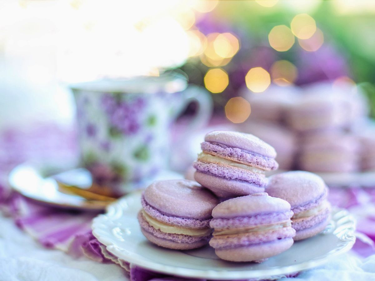 A plate of lavender-colored macarons with a floral tea cup in the background.