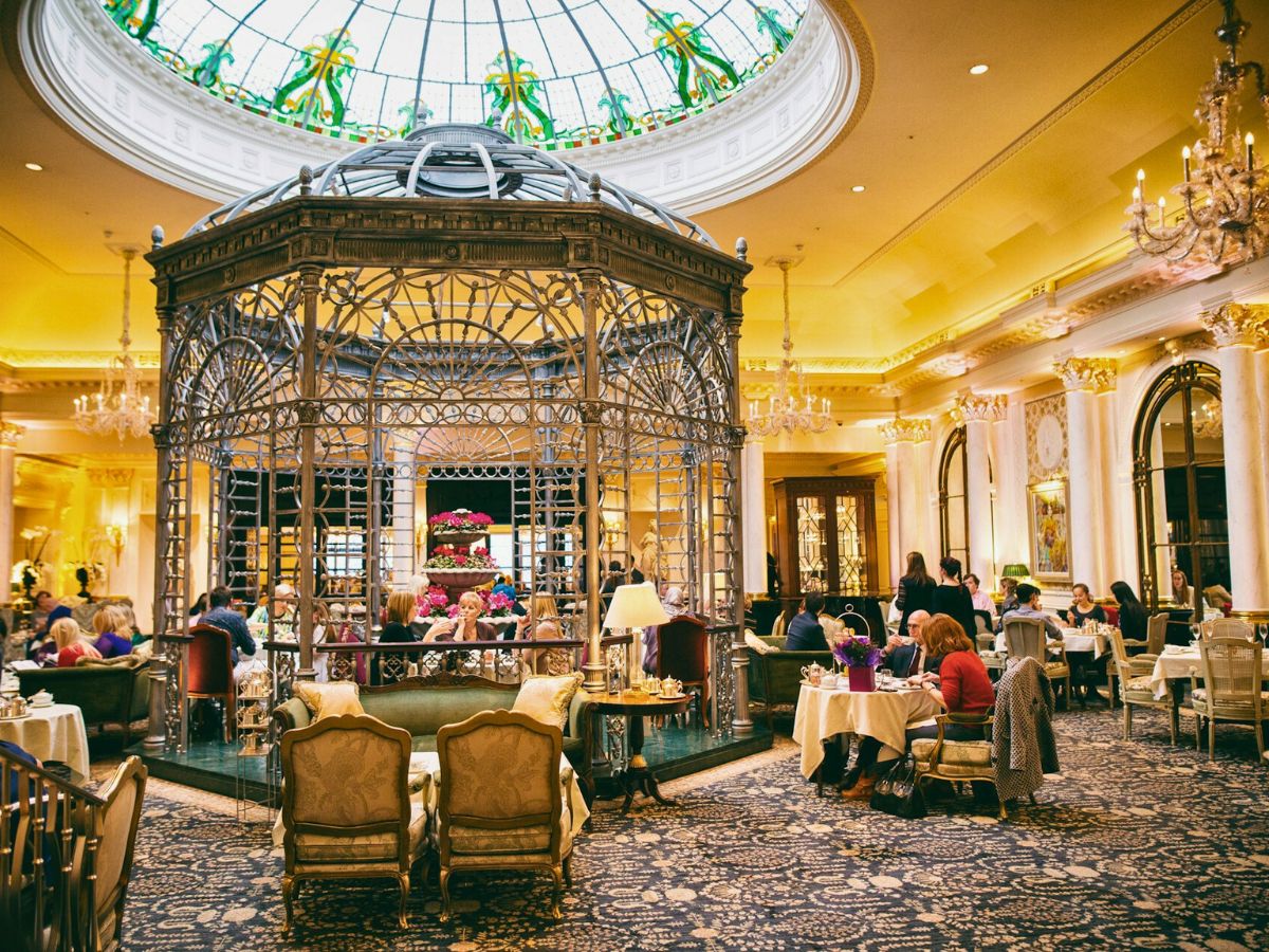 A luxurious dining area with patrons seated at tables, featuring an ornate metal gazebo under a large glass dome.