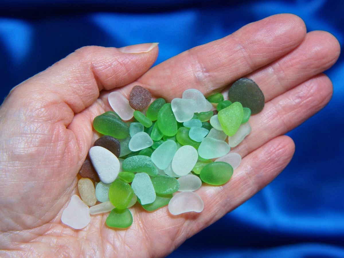 A hand holding a collection of colorful, smooth sea glass pieces above a blue background.