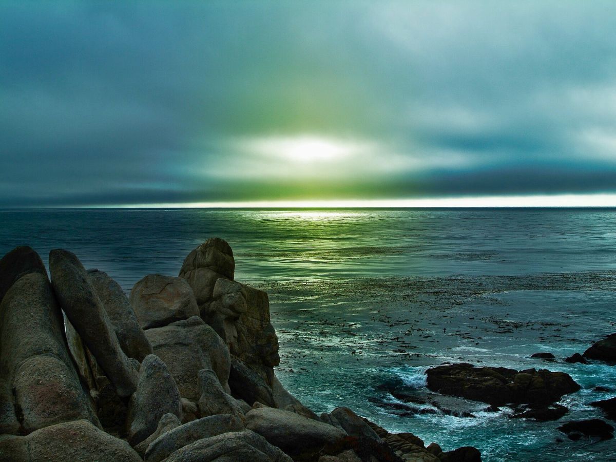 Sunlight filtering through cloudy skies over a rocky coastline.