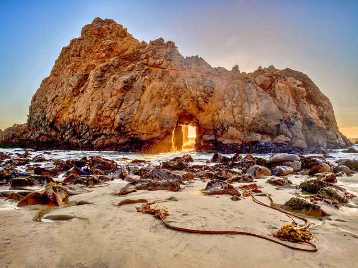 Rocky beach at sunset with light shining through a natural arch in the rock formation.