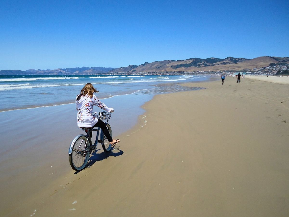 A person riding a bicycle along the shoreline on a sunny beach day.