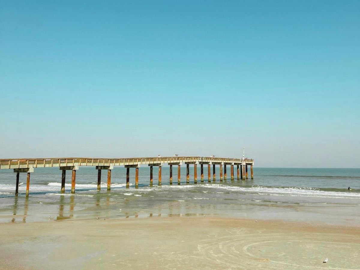 A long wooden pier extending into the sea under a clear blue sky.