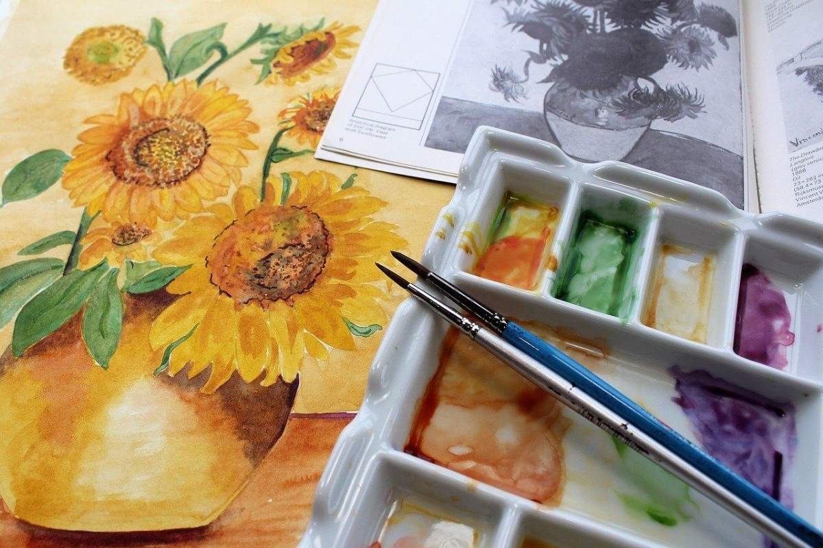 Art supplies and a sunflower painting next to an open book.