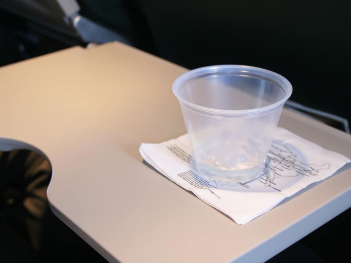 A plastic cup with a small amount of water, on a napkin with a map design, placed on an airplane tray table.