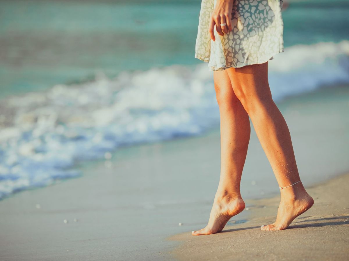 A person walking barefoot along the shoreline with the ocean in the background.