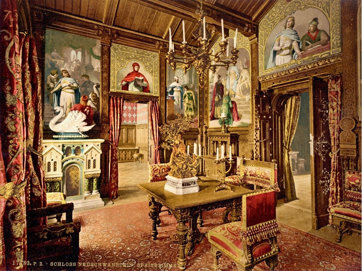 A richly decorated historical room with ornate furniture, elaborate chandeliers, and large murals on the walls. The room has a red carpet and tapestries, combining medieval and regal design elements.