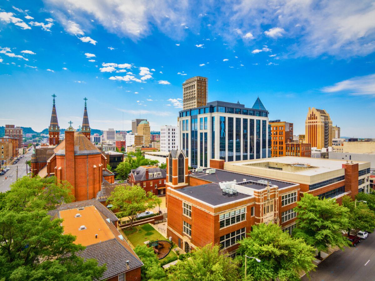 A cityscape view of Downtown Birmingham Alabama featuring a mix of modern and historic buildings under a clear blue sky with scattered clouds.
