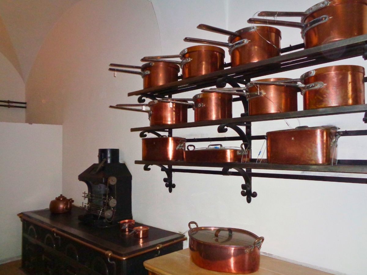 A kitchen with copper pots and pans arranged on metal shelves above a black cooking stove.