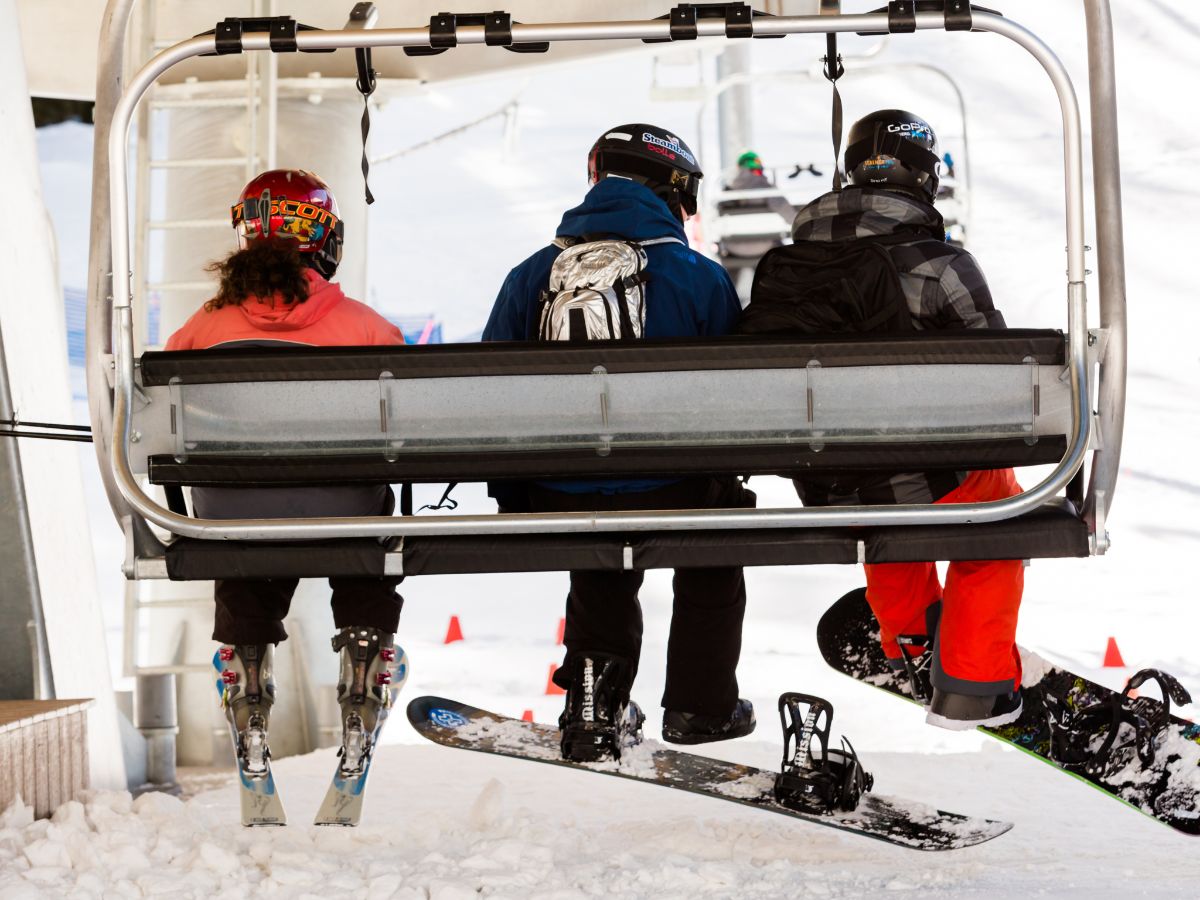 Three people in ski and snowboard gear ride up a snowy slope on a ski lift.