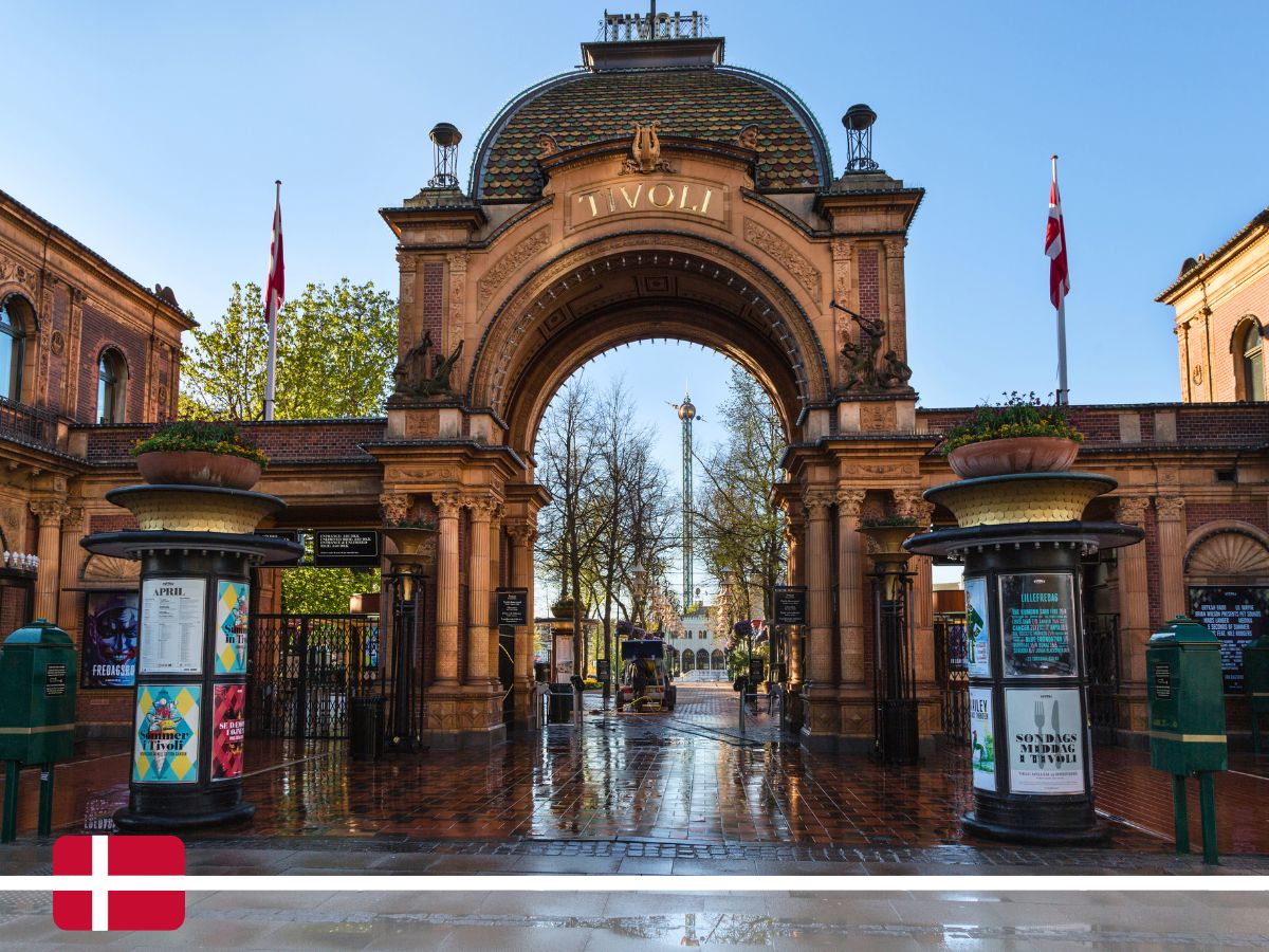 The entrance to Tivoli Gardens in Copenhagen, Denmark, featuring an ornate archway with flags flying and a clear sky in the background.