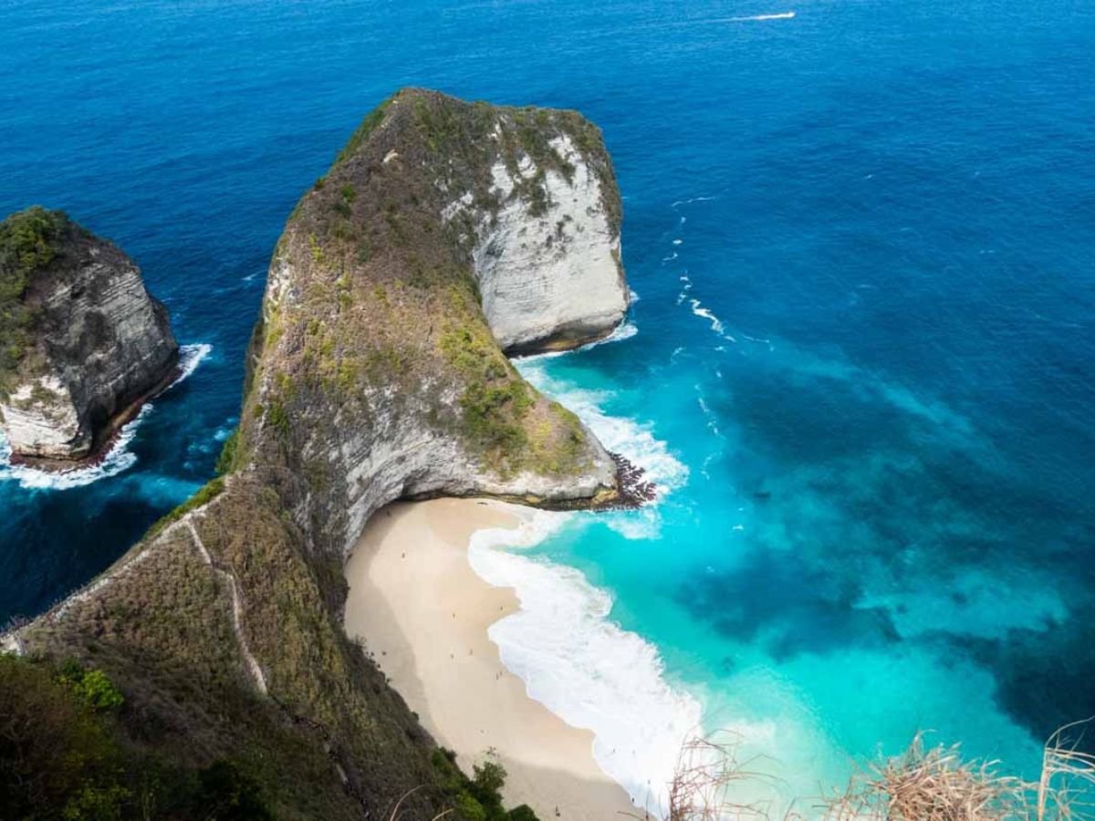 Aerial view of a secluded beach surrounded by steep, rocky cliffs and turquoise waves crashing onto the shore.