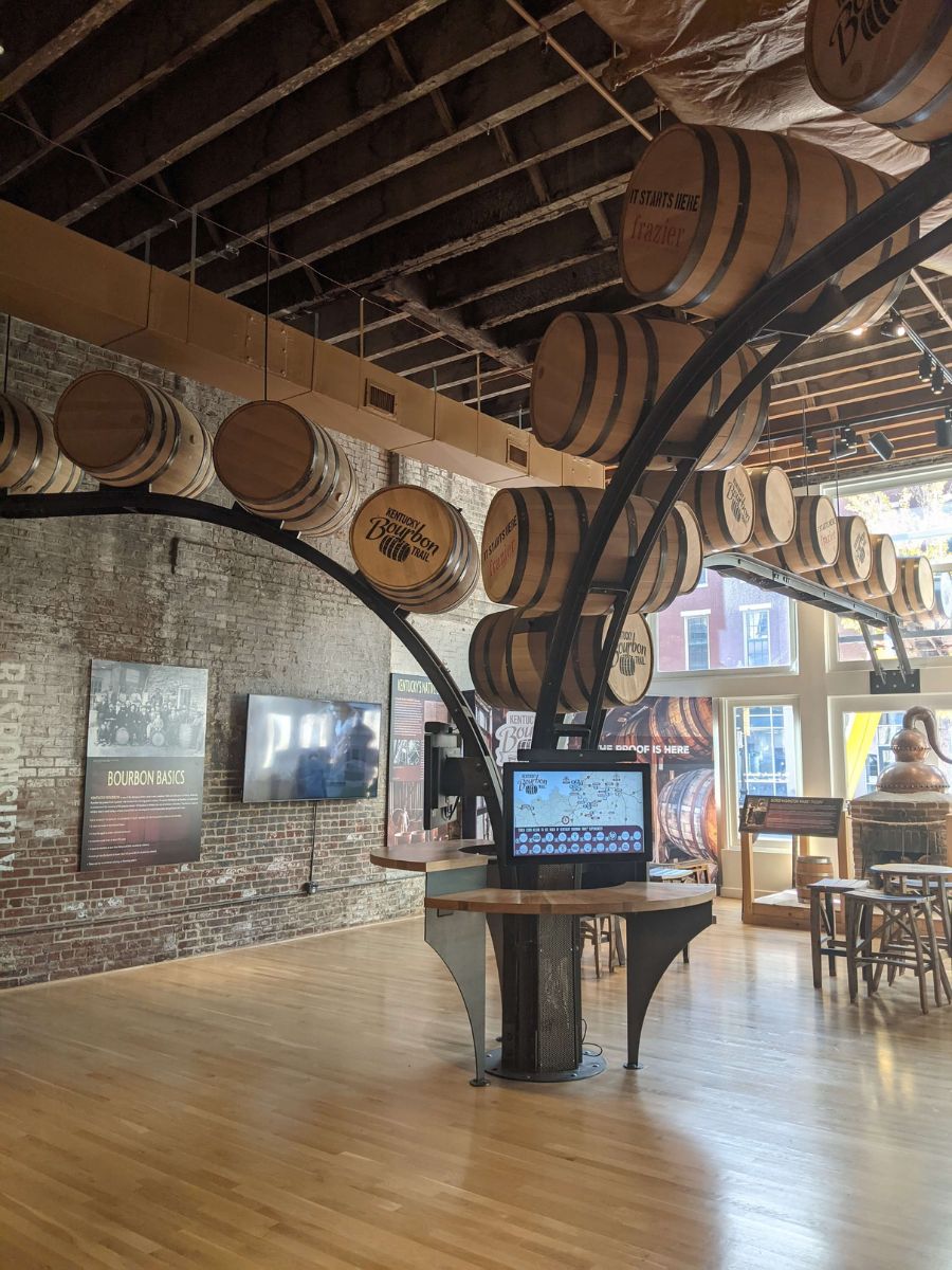 Interior of a barrel-themed distillery with wooden floors, exposed brick walls, a large central structure holding barrels, and a wooden barrel display at the back.