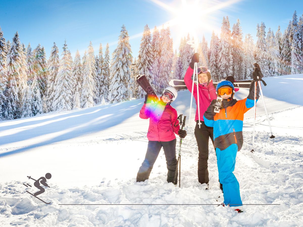 Three people in winter clothing standing on a snowy slope, holding ski poles and gear, with a forest and bright sun in the background.