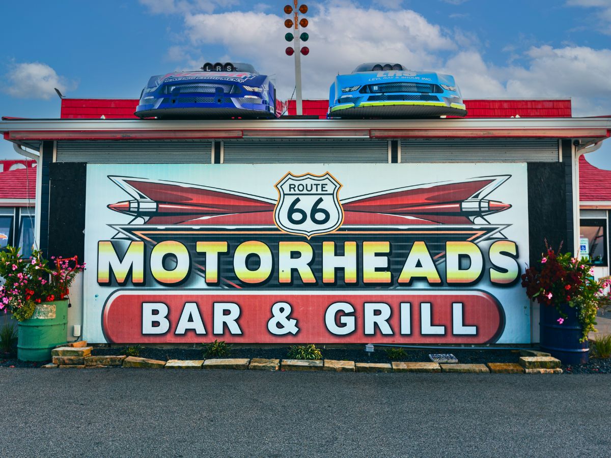 Exterior of Motorheads Bar & Grill featuring a Route 66 sign and two race cars on the roof.